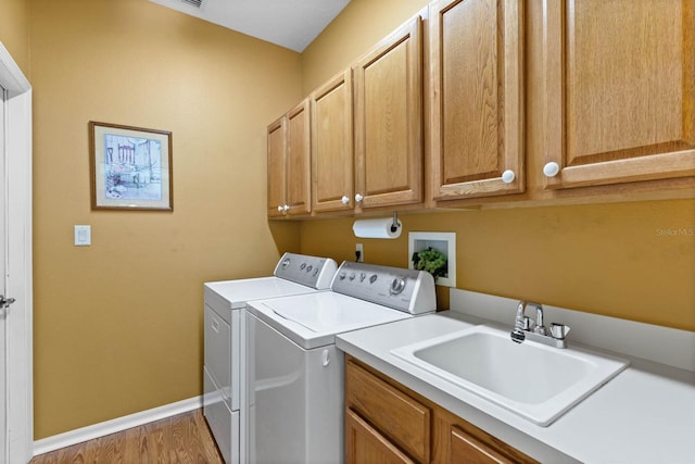 clothes washing area with washer and dryer, cabinets, sink, and light hardwood / wood-style flooring