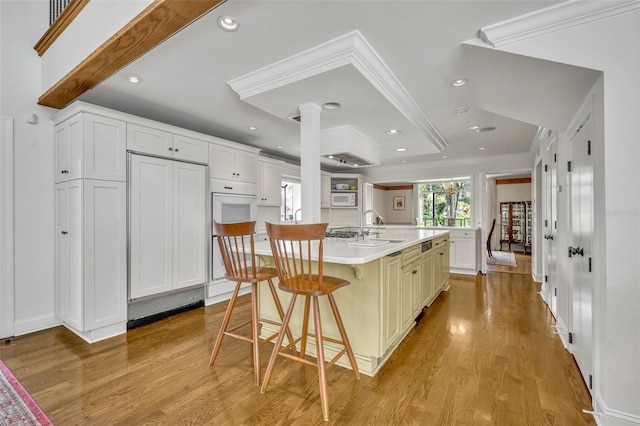 kitchen featuring white cabinets, sink, an island with sink, a kitchen breakfast bar, and light hardwood / wood-style floors