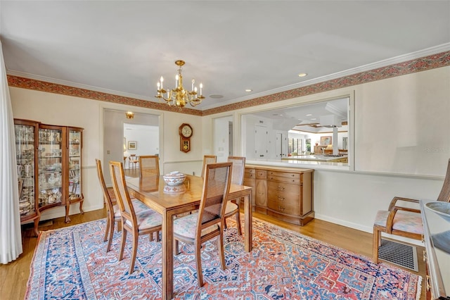 dining area with a chandelier, light wood-type flooring, and ornamental molding