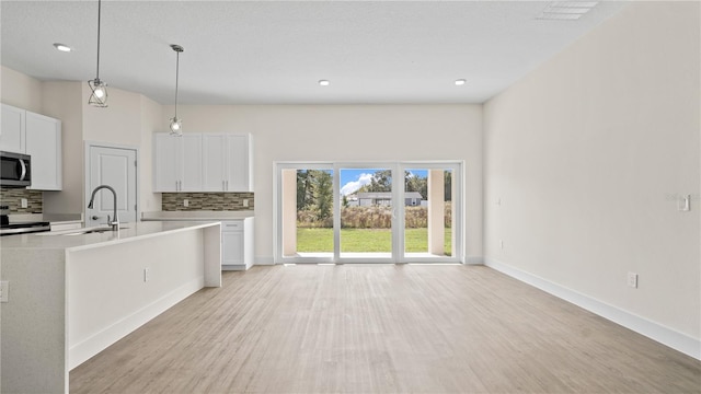 kitchen with white cabinets, light hardwood / wood-style flooring, decorative light fixtures, and backsplash