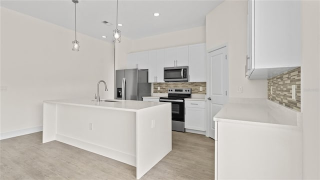 kitchen featuring stainless steel appliances, hanging light fixtures, sink, an island with sink, and white cabinets