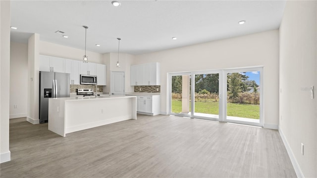 kitchen featuring stainless steel appliances, white cabinets, an island with sink, light wood-type flooring, and decorative light fixtures