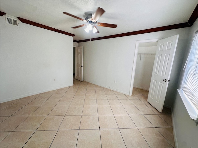 unfurnished bedroom with ceiling fan, light tile patterned floors, a walk in closet, crown molding, and a closet