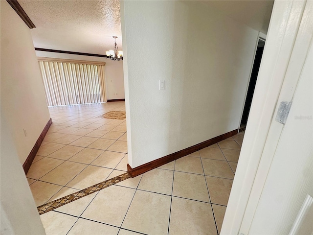 corridor featuring a chandelier, a textured ceiling, light tile patterned floors, and crown molding