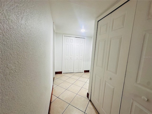 hallway with a textured ceiling and light tile patterned floors