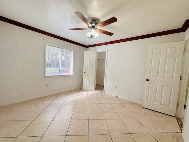 unfurnished bedroom featuring a textured ceiling, light tile patterned floors, ceiling fan, crown molding, and a spacious closet