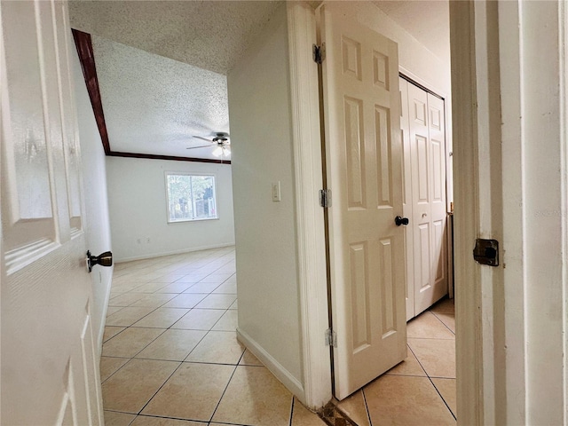 hall featuring a textured ceiling, light tile patterned floors, and ornamental molding