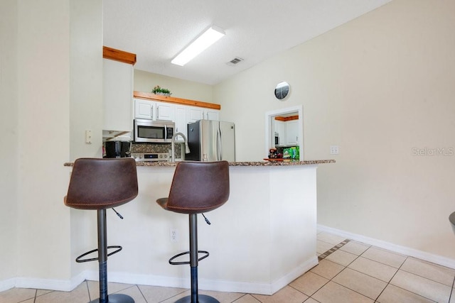 kitchen with stainless steel appliances, white cabinetry, kitchen peninsula, a kitchen breakfast bar, and light tile patterned floors