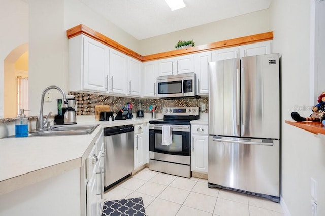 kitchen featuring stainless steel appliances, light tile patterned flooring, sink, backsplash, and white cabinets