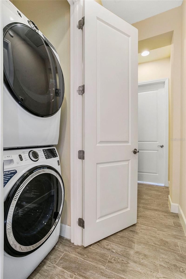 washroom with stacked washer / drying machine and light hardwood / wood-style flooring