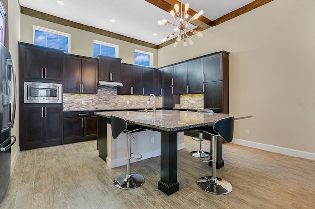 kitchen with a kitchen breakfast bar, light stone counters, light hardwood / wood-style flooring, an island with sink, and appliances with stainless steel finishes