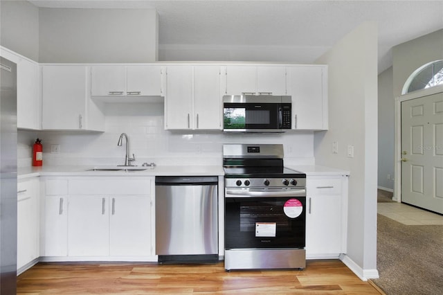 kitchen featuring stainless steel appliances, sink, tasteful backsplash, white cabinetry, and light hardwood / wood-style flooring