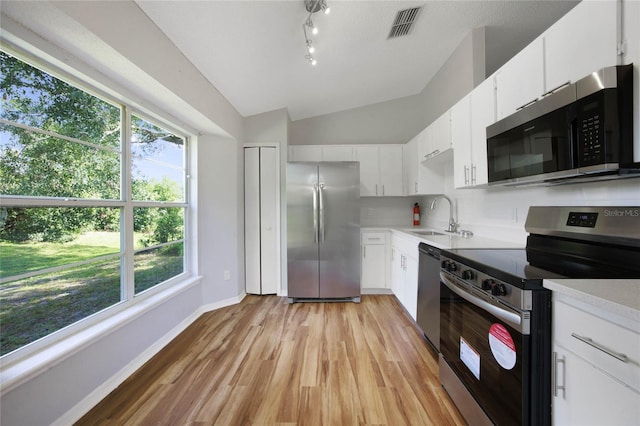 kitchen with stainless steel appliances, white cabinetry, a healthy amount of sunlight, and lofted ceiling