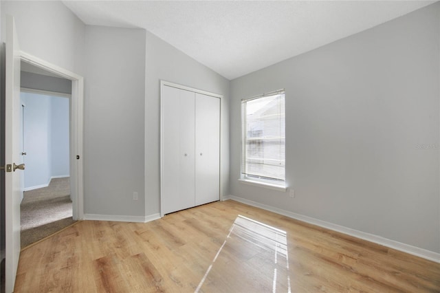 unfurnished bedroom with a closet, light wood-type flooring, and lofted ceiling