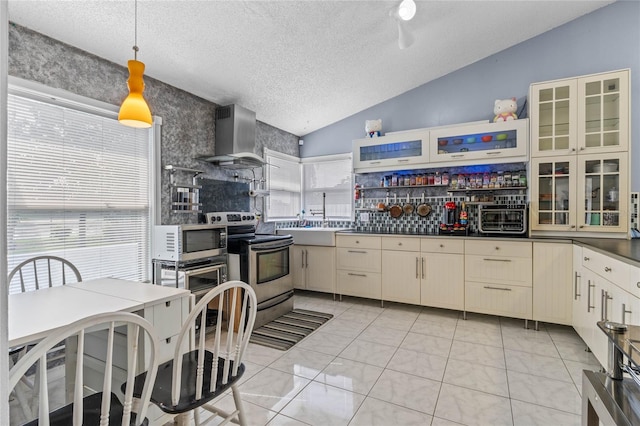 kitchen with appliances with stainless steel finishes, cream cabinets, a textured ceiling, and wall chimney range hood