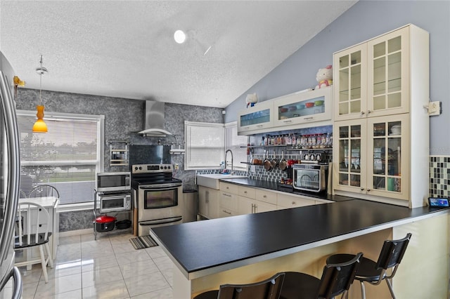 kitchen with appliances with stainless steel finishes, a textured ceiling, pendant lighting, sink, and wall chimney exhaust hood