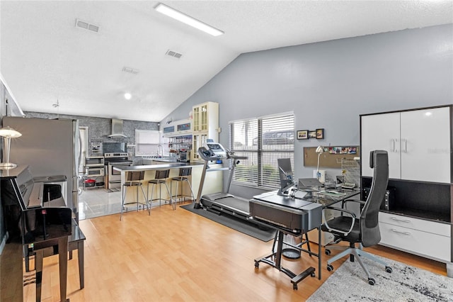 office area featuring light wood-type flooring, vaulted ceiling, and a textured ceiling