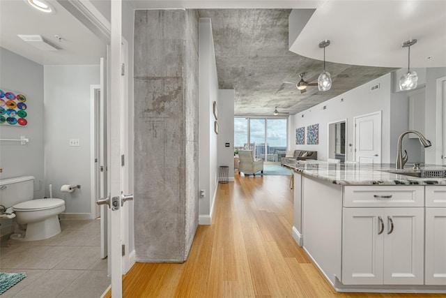 kitchen featuring light hardwood / wood-style floors, light stone counters, hanging light fixtures, sink, and white cabinetry