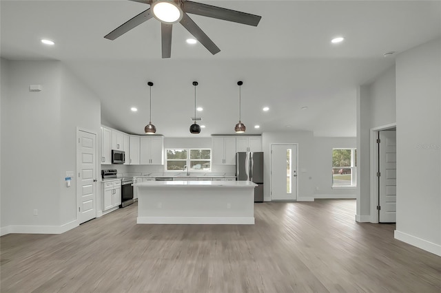 kitchen with white cabinetry, pendant lighting, a kitchen island, light wood-type flooring, and stainless steel appliances