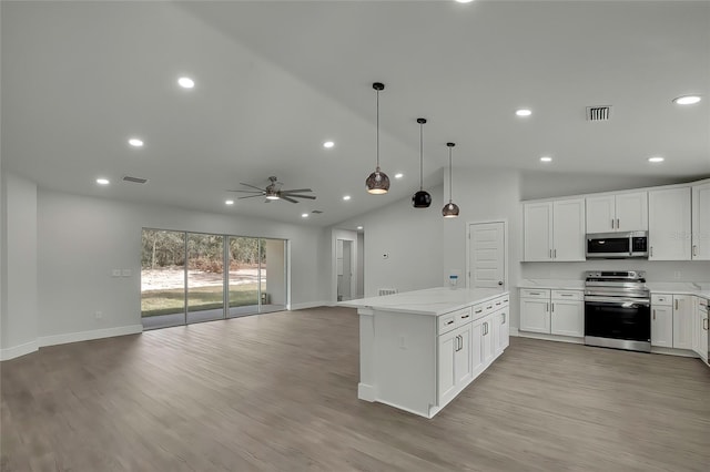 kitchen with white cabinets, a kitchen island, appliances with stainless steel finishes, decorative light fixtures, and light wood-type flooring