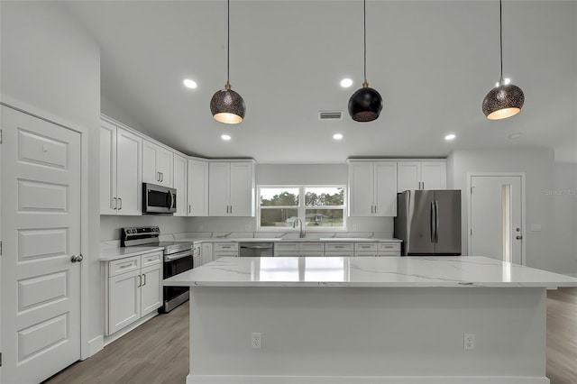 kitchen with light stone countertops, appliances with stainless steel finishes, pendant lighting, a center island, and white cabinetry