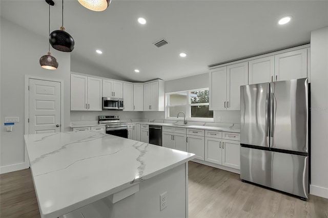 kitchen featuring white cabinets, pendant lighting, lofted ceiling, stainless steel appliances, and light stone counters