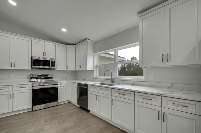 kitchen with appliances with stainless steel finishes, light hardwood / wood-style flooring, white cabinetry, and sink