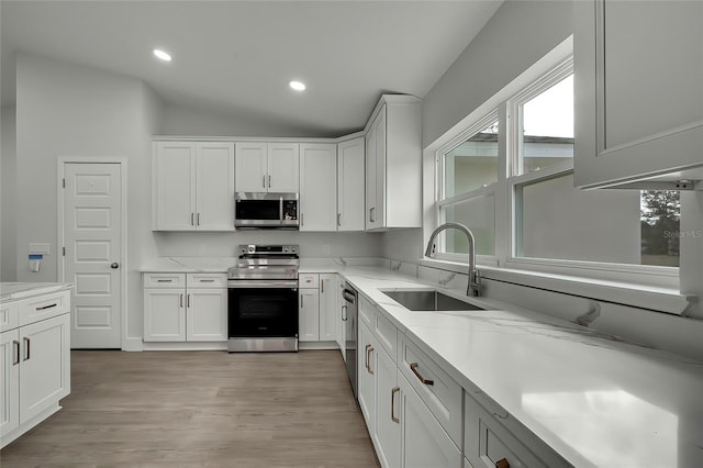 kitchen featuring white cabinetry, sink, vaulted ceiling, appliances with stainless steel finishes, and light wood-type flooring