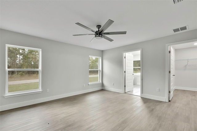 unfurnished bedroom featuring a walk in closet, ensuite bathroom, a closet, ceiling fan, and light wood-type flooring