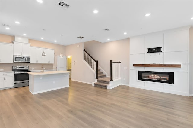 kitchen featuring white cabinets, light wood-type flooring, stainless steel appliances, and an island with sink