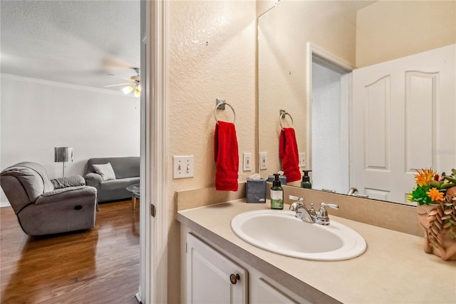 bathroom with vanity, ceiling fan, ornamental molding, a textured ceiling, and wood-type flooring