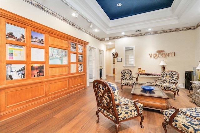 sitting room with rail lighting, a raised ceiling, wood-type flooring, and ornamental molding