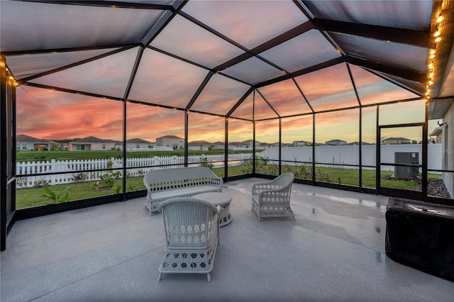 patio terrace at dusk featuring a lawn, glass enclosure, and a water view