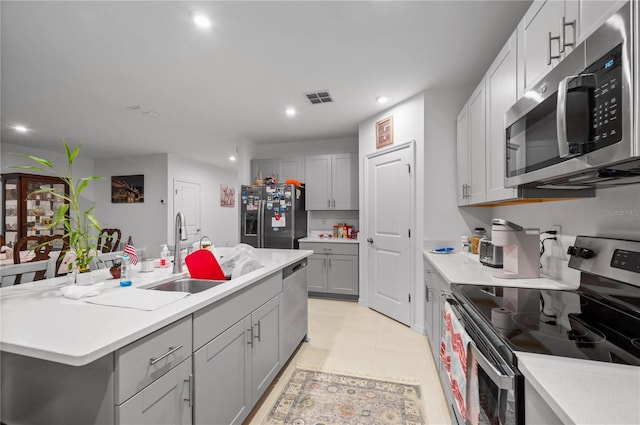 kitchen featuring stainless steel appliances, gray cabinets, an island with sink, and sink