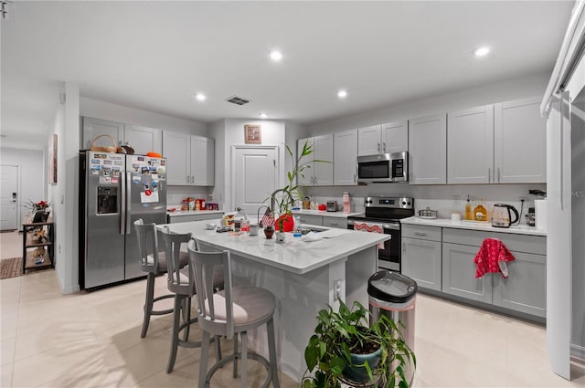 kitchen with stainless steel appliances, gray cabinetry, light tile patterned floors, and a kitchen island with sink