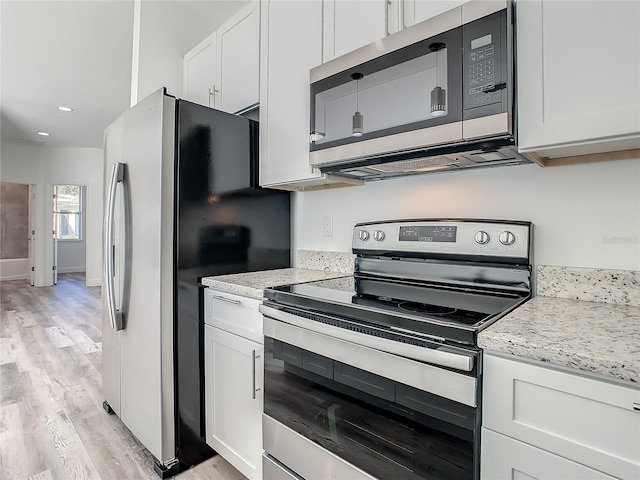 kitchen with white cabinets, light stone counters, light wood-type flooring, and appliances with stainless steel finishes