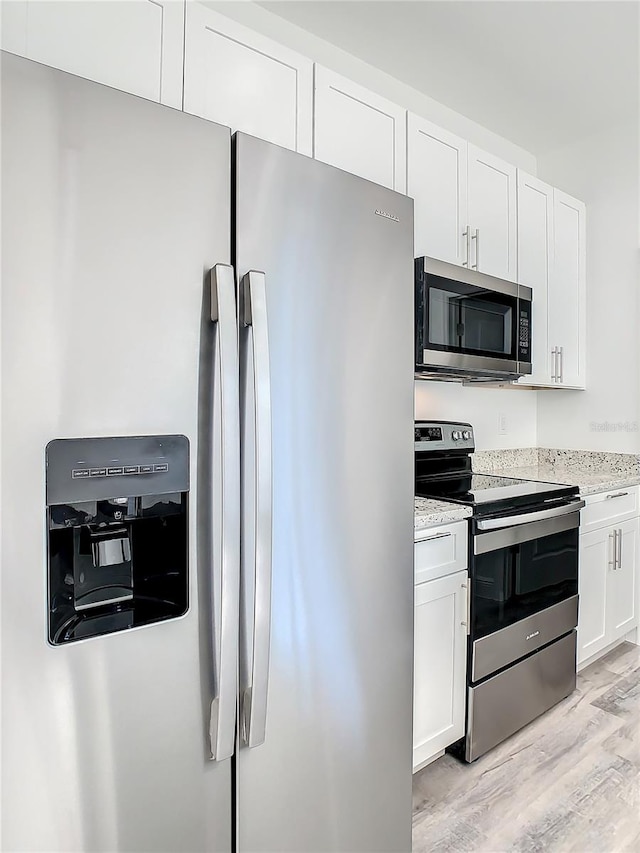 kitchen featuring light stone counters, white cabinetry, light wood-type flooring, and appliances with stainless steel finishes