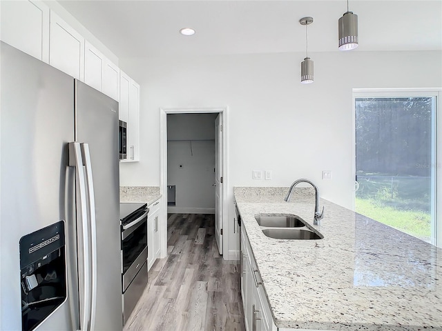 kitchen with stainless steel appliances, light stone counters, pendant lighting, sink, and white cabinetry