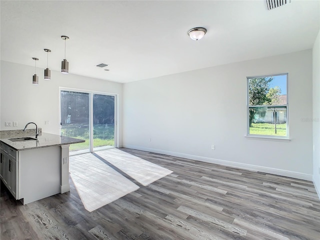 interior space featuring light stone counters, kitchen peninsula, sink, dark hardwood / wood-style floors, and pendant lighting