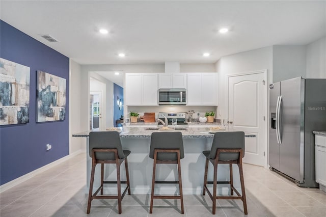 kitchen with stainless steel appliances, white cabinets, a kitchen island with sink, and light stone counters