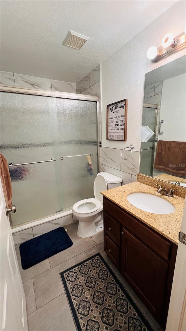 bathroom featuring tile patterned floors, a textured ceiling, toilet, vanity, and a shower with shower door