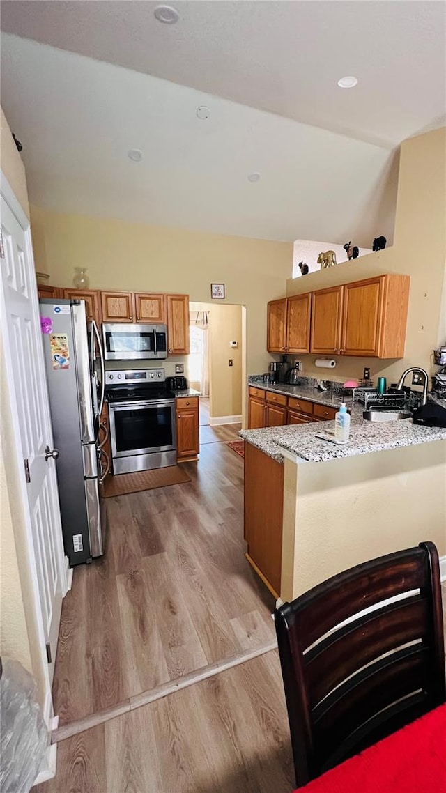 kitchen with sink, appliances with stainless steel finishes, light hardwood / wood-style floors, light stone counters, and kitchen peninsula