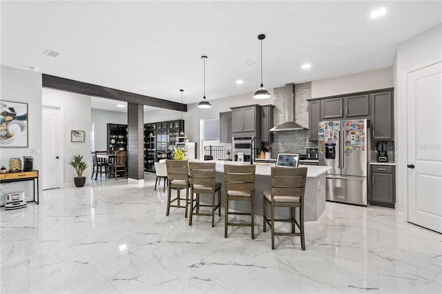 kitchen featuring gray cabinets, stainless steel appliances, wall chimney exhaust hood, and a center island with sink