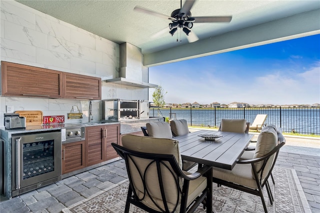 view of patio with an outdoor kitchen, ceiling fan, beverage cooler, and a water view