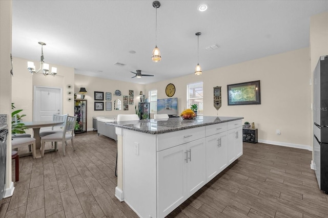 kitchen featuring dark hardwood / wood-style flooring, dark stone counters, pendant lighting, white cabinets, and a center island