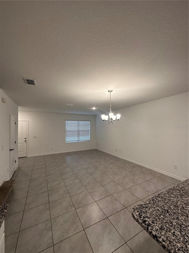 tiled spare room featuring a textured ceiling and an inviting chandelier