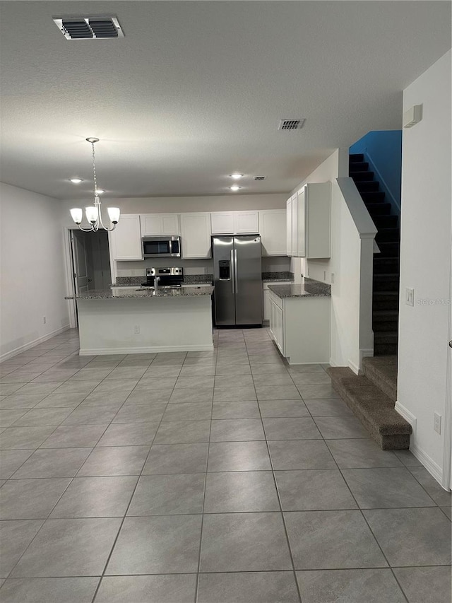 kitchen featuring dark stone counters, decorative light fixtures, white cabinetry, stainless steel appliances, and a chandelier