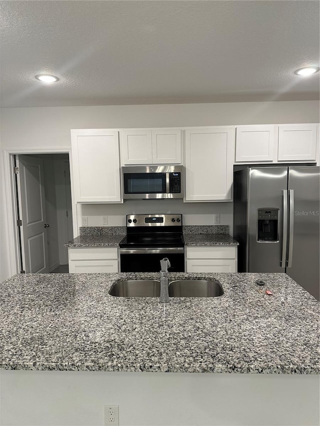 kitchen with stone counters, appliances with stainless steel finishes, white cabinetry, and sink