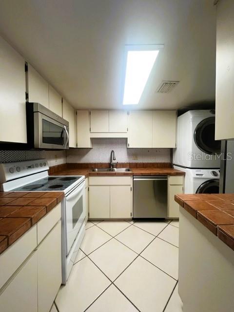 kitchen with white cabinets, stacked washer and dryer, sink, and appliances with stainless steel finishes