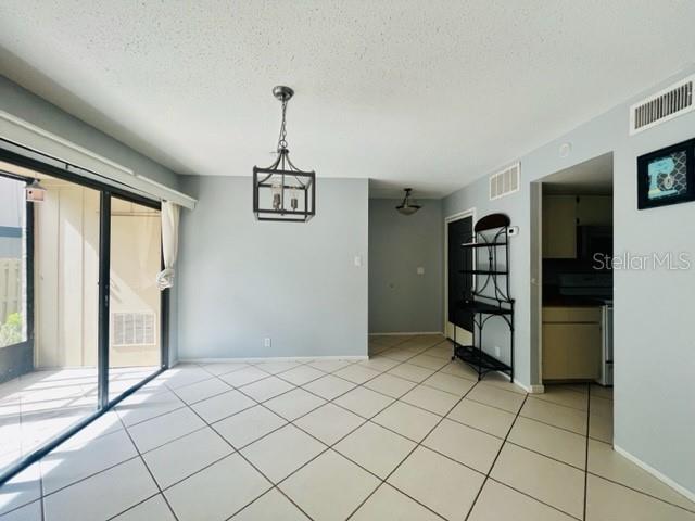 spare room featuring a notable chandelier, a textured ceiling, and light tile patterned floors